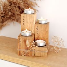 three wooden blocks with candles sitting on top of each other in front of a dried plant