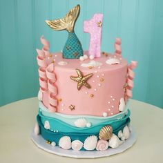 a pink and blue birthday cake decorated with mermaid tail, starfish, seashells and the number one