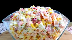 a glass bowl filled with corn salad on top of a wooden table