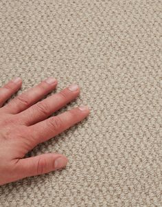 a person's hand on top of a beige carpet