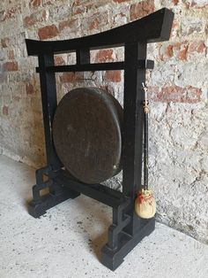 an old black clock with a pendulum on it's stand in front of a brick wall