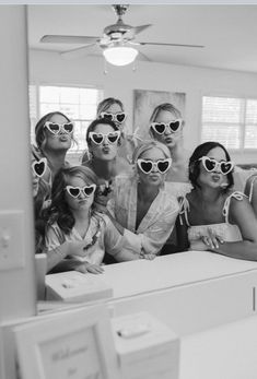 a black and white photo of women wearing heart - shaped sunglasses in front of a mirror