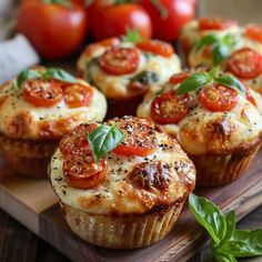 several small muffins with tomatoes and basil on top sitting on a cutting board