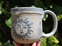 a hand holding a ceramic mug with sun and moon designs on it's side