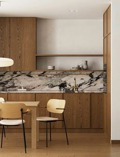 a modern kitchen with marble counter tops and wooden cabinets, along with two dining chairs