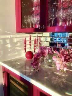 some pink flowers are in a vase on the kitchen counter with wine glasses and candles