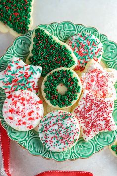 decorated cookies on a green plate with red and white sprinkles next to a red ribbon