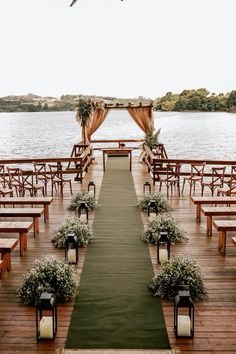 an outdoor ceremony setup with wooden benches and greenery on the aisle, overlooking water