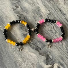 two beaded bracelets with black, yellow and pink beads on a marble surface