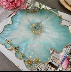 a large blue flower shaped tray with gold trimmings and flowers in the background