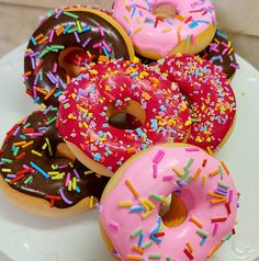 three donuts with pink frosting and sprinkles on a white plate