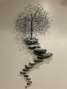 a metal tree with rocks on the bottom and a rock path in front of it