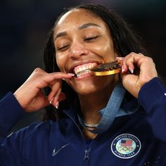 a woman is smiling while holding a gold medal in her mouth