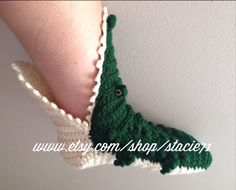 a pair of crocheted alligator slippers are hanging on the wall, one is green and the other is white