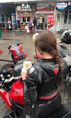 a woman is sitting on a red motorcycle and holding a cup in her hand while looking at the camera