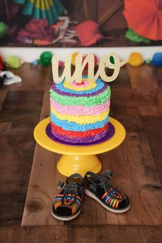 a colorful cake with the word uno spelled on top and two pairs of shoes sitting next to it