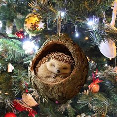 a hedgehog curled up in a hollow log ornament hanging from a christmas tree