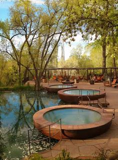 an outdoor swimming pool surrounded by trees and water features circular seating around the edge with chairs on either side