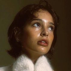 a woman with short hair wearing a white turtle neck sweater and looking off to the side