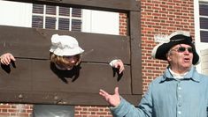 two people dressed in colonial garb standing next to a wooden door with their hands out