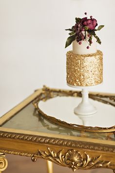 a white and gold wedding cake sitting on top of a table next to a mirror