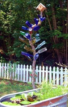 a metal planter filled with blue glass bottles and plants in front of a white picket fence