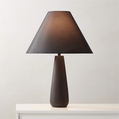 a table lamp with a black shade on it sitting on a white shelf next to a gray wall