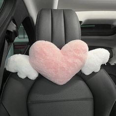 a pink heart shaped pillow sitting on the back seat of a car with angel wings