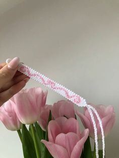 a hand is holding a white string with pink flowers in it and some tulips