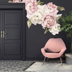 a pink chair sitting in front of a black door with flowers on the wall behind it