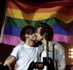 two young men kissing each other in front of a rainbow - colored flag and microphone