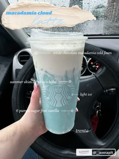 the starbucks drink is being held up by someone's hand in front of their car