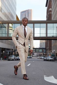 a man in a tan suit and brown shoes walking down the street with his hands on his hips