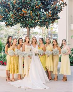 a group of women standing next to each other holding bouquets in front of a tree