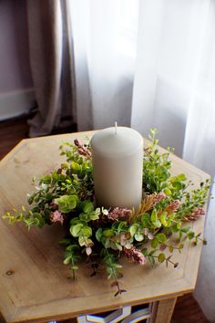 a white candle sitting on top of a wooden table next to a planter filled with greenery