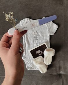 a person holding a toothbrush next to a baby's bodysuit and other items