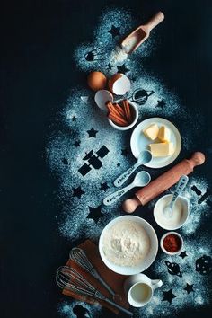 an assortment of ingredients are shown on a black surface with flour, eggs, butter and cinnamon sticks