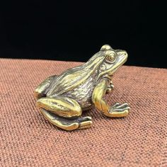 a gold colored frog sitting on top of a brown cloth