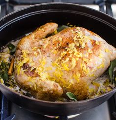 a chicken in a skillet on top of the stove with herbs and spices around it