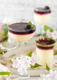 two glasses filled with dessert sitting on top of a plate next to flowers and leaves