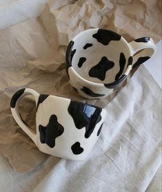 two black and white cow print coffee mugs sitting on top of a piece of paper