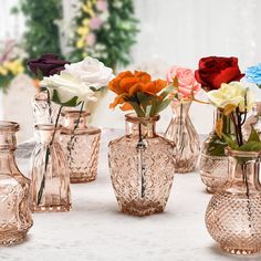 there are many different colored flowers in vases on the tablecloth with white cloth