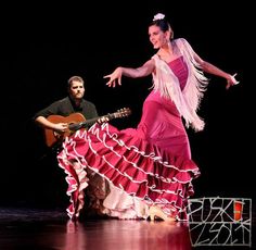 a woman in a pink dress is dancing with a man playing guitar behind her on stage