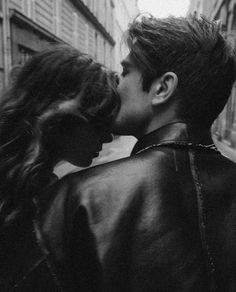 black and white photograph of two people kissing in the street with buildings in the background