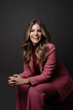 a woman sitting on top of a chair in a red suit and smiling at the camera