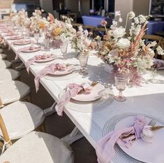 the table is set with pink and white flowers in vases, plates and napkins