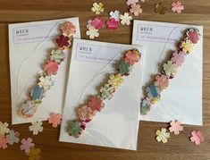 three pieces of paper with flowers on them sitting next to some cards and confetti