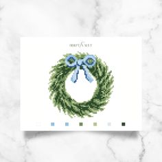 a cross stitch christmas card with a green wreath and blue bow on it's front