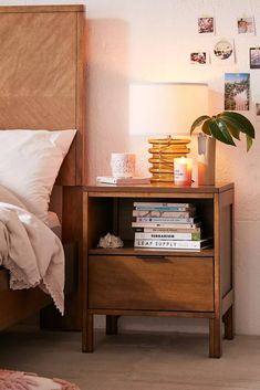 a nightstand with books and candles on it next to a bed