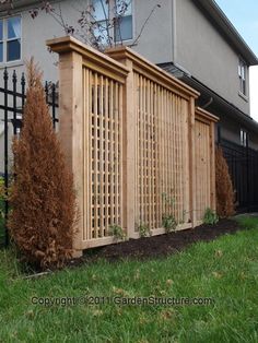 a wooden fence in front of a house with green grass and bushes next to it